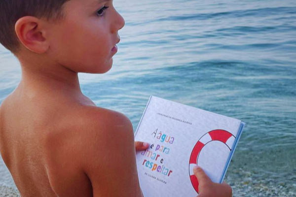 menino com o livro agua e para amar e respeitar junto ao mar